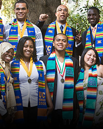 Group of people smiling together outside in front of a tree for a group photo
